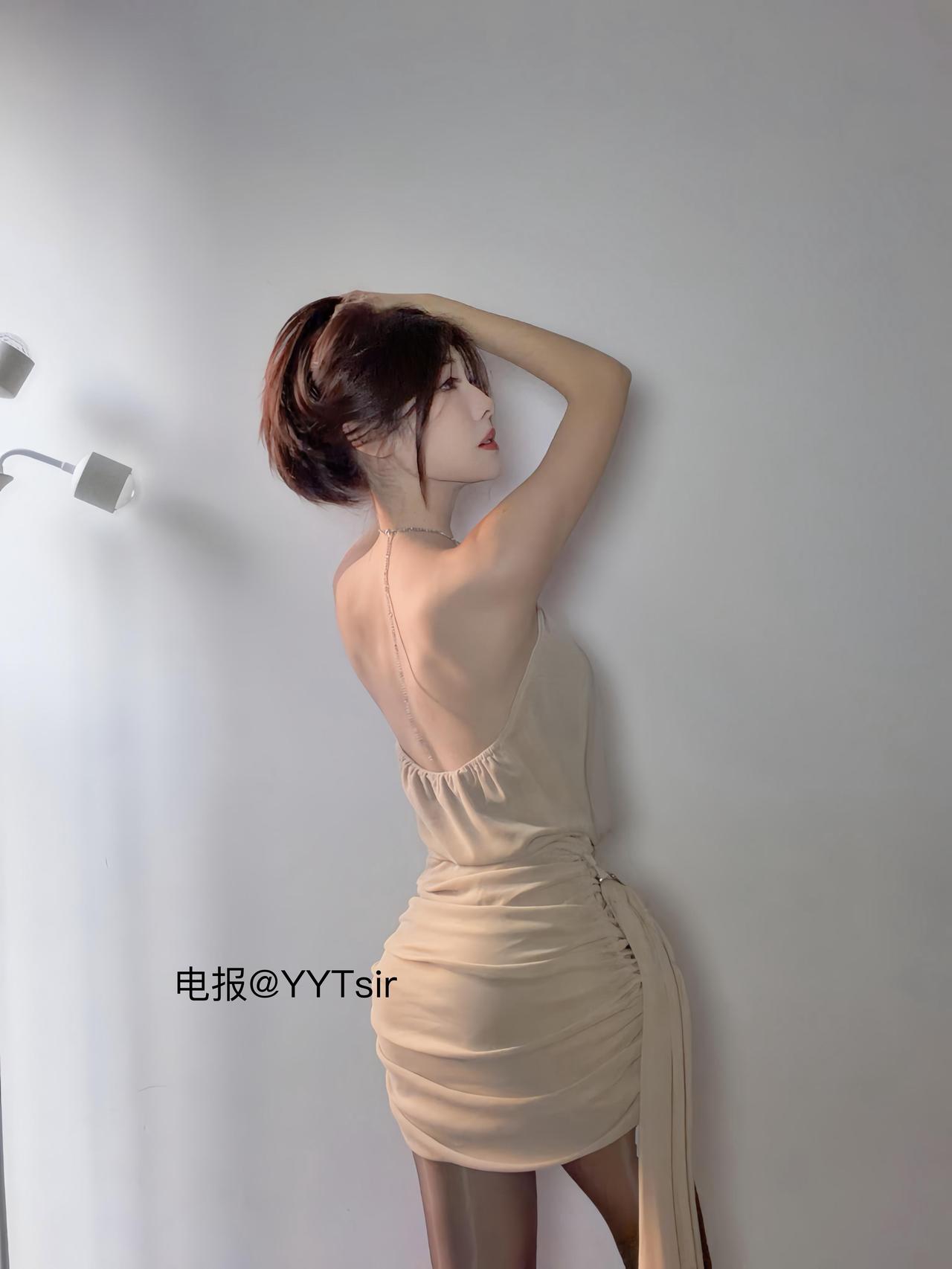 木木ivy 米色挂脖连衣裙、白墙前的背面举臂姿势