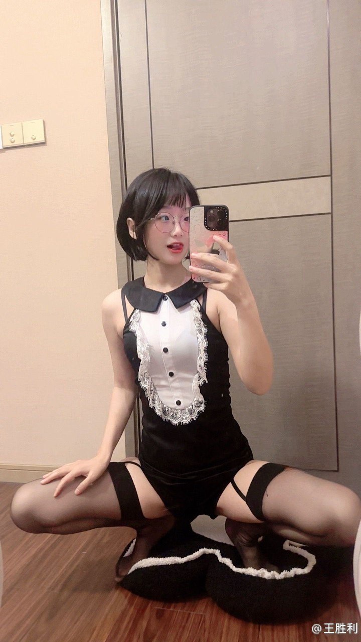 王胜利黑白翻领衣装镜面坐姿，背景为木色门板