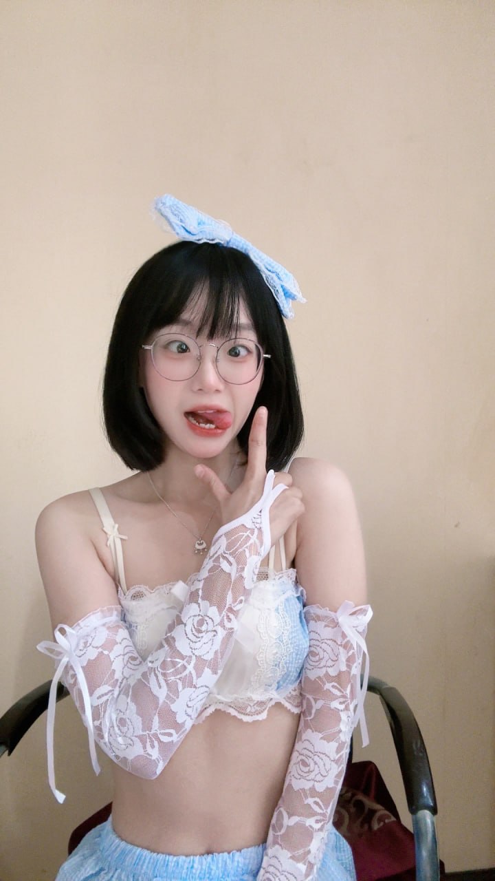 王胜利浅蓝发饰与白色蕾丝衣装近景，圆框眼镜映衬浅墙