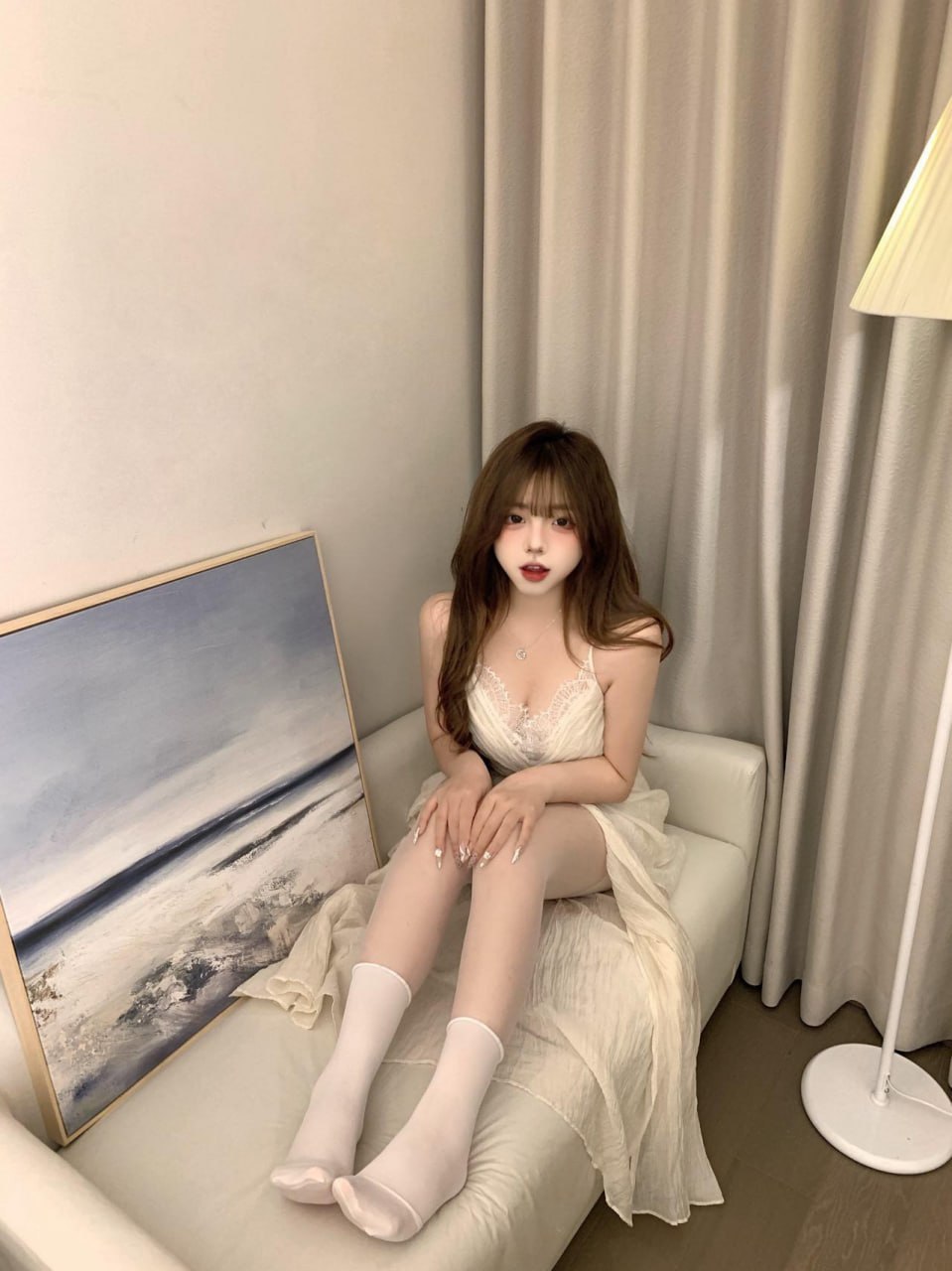 小猫困困穿浅色花纹长裙坐在灰帘前的奶油色沙发上