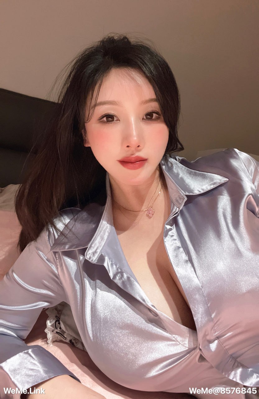 紫色哒豚豚 穿浅色亮面翻领上衣侧身靠在床边，胸前有项链
